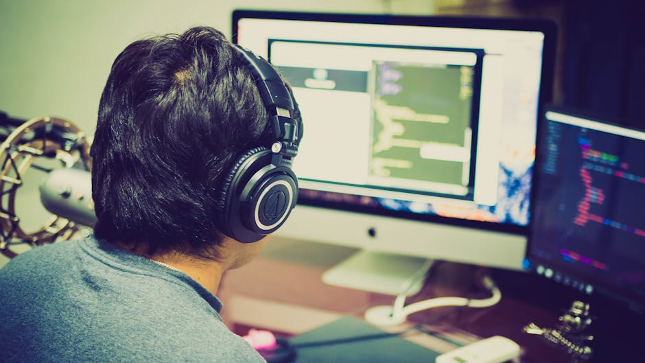 A programmer with headphones focuses on coding at a computer setup
