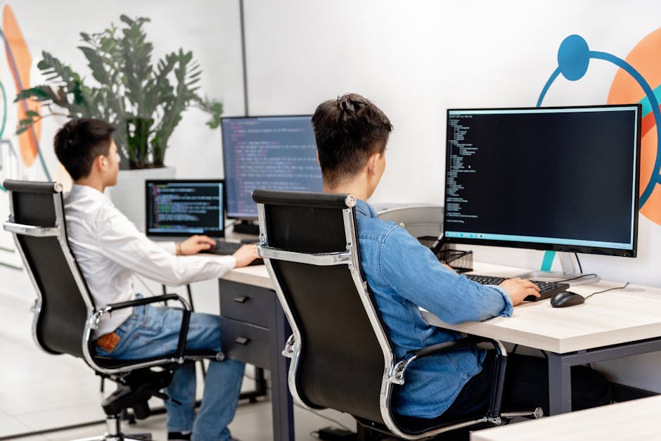 Two male developers at desks programming in a modern office workspace